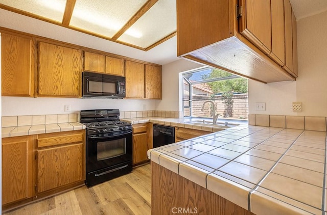 43920 Delgado Ct, Lancaster, CA 93535 - kitchen with black appliances, tile counters, light wood-style flooring, and brown cabinetry