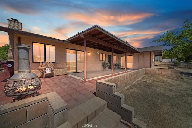 7575 Whitney Ave, Yucca Valley, CA 92284 - back of property at dusk with an outdoor fire pit, a patio area, a chimney, and stucco siding