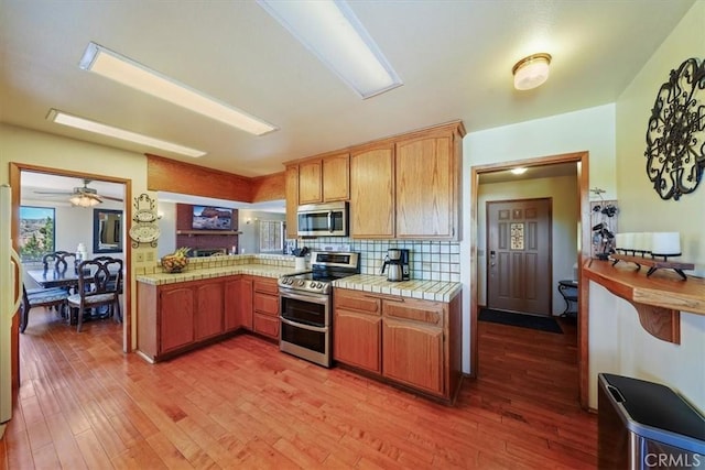 7575 Whitney Ave, Yucca Valley, CA 92284 - kitchen featuring appliances with stainless steel finishes, light wood finished floors, tile countertops, backsplash, and ceiling fan