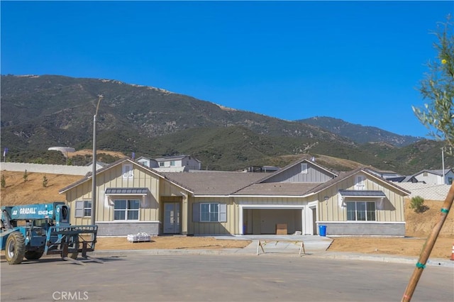7051 Hurley Ct, San Bernardino, CA 92407 - view of front of house featuring board and batten siding, a mountain view, a garage, and driveway