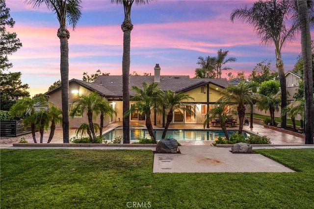 5829 Zapata Pl, Rancho Cucamonga, CA 91737 - back of property at dusk with a patio, stucco siding, a yard, a chimney, and an outdoor pool
