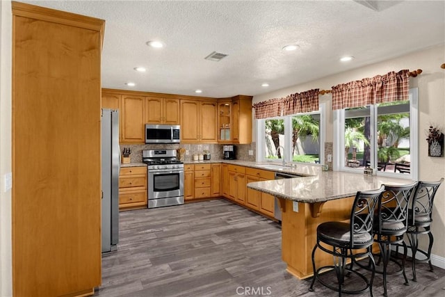 5829 Zapata Pl, Rancho Cucamonga, CA 91737 - kitchen with stainless steel appliances, a peninsula, wood finished floors, tasteful backsplash, and light stone countertops