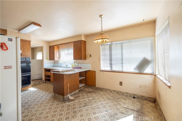 3142 Keith Ave, Castro Valley, CA 94546 - kitchen featuring a peninsula, brown cabinetry, light countertops, pendant lighting, and freestanding refrigerator