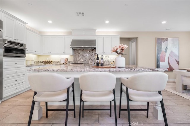 111 Spoke, Irvine, CA 92618 - kitchen featuring under cabinet range hood, oven, white cabinets, backsplash, and a kitchen bar