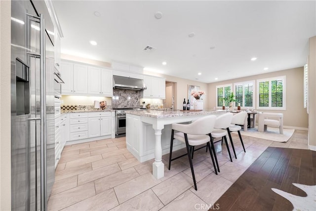 111 Spoke, Irvine, CA 92618 - kitchen with high end appliances, under cabinet range hood, a kitchen bar, backsplash, and white cabinetry