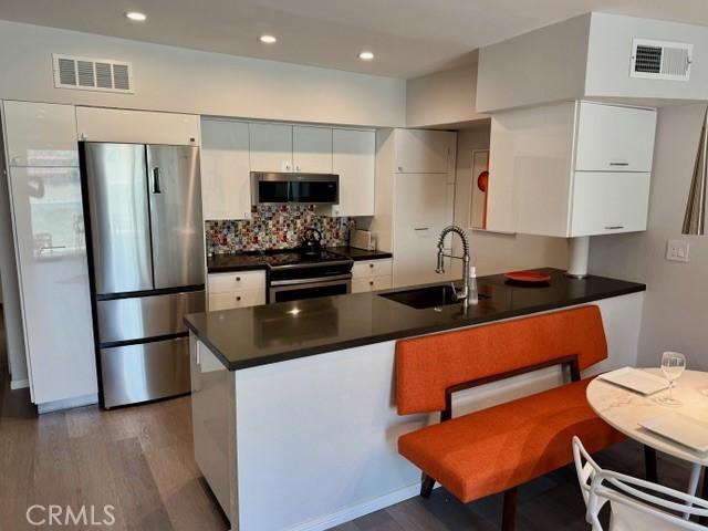 1655 E Palm Canyon Dr Unit 308, Palm Springs, CA 92264 - kitchen featuring appliances with stainless steel finishes, a peninsula, dark countertops, wood finished floors, and white cabinets