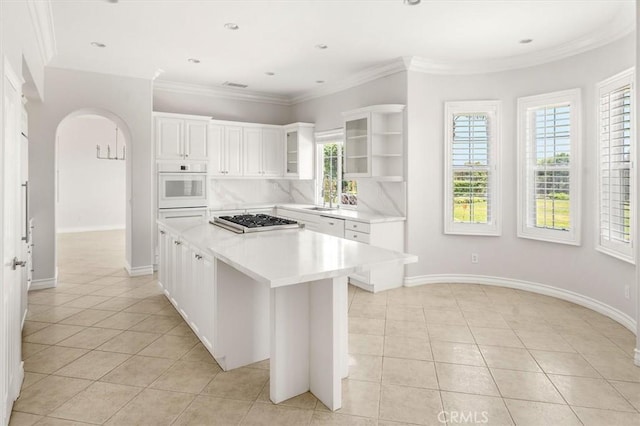 24711 Tiburon St, Valencia, CA 91355 - kitchen featuring white appliances, light tile patterned floors, a center island, arched walkways, and crown molding