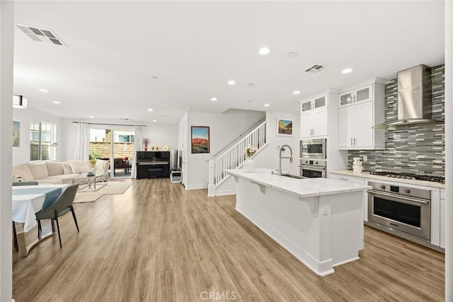 12260 Chorus Dr, Rancho Cucamonga, CA 91739 - kitchen featuring appliances with stainless steel finishes, wall chimney exhaust hood, open floor plan, backsplash, and light wood finished floors