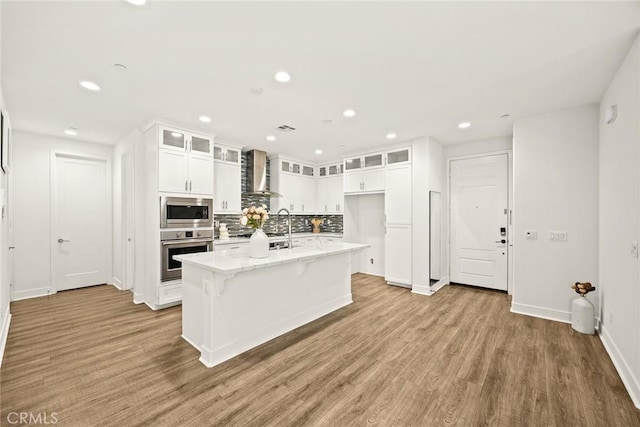12260 Chorus Dr, Rancho Cucamonga, CA 91739 - kitchen featuring stainless steel appliances, wall chimney exhaust hood, white cabinets, tasteful backsplash, and wood finished floors