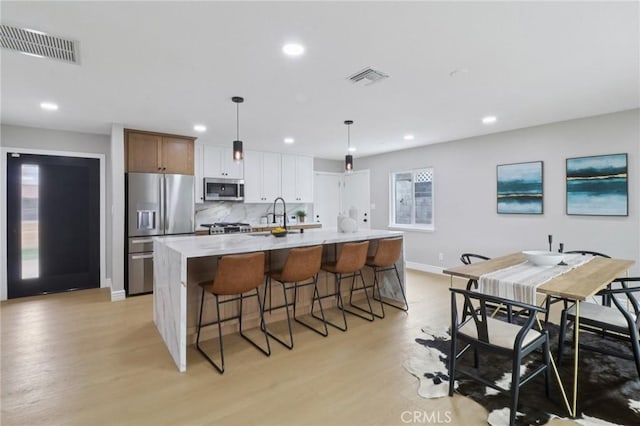 4203 Tolowa St, San Diego, CA 92117 - kitchen featuring stainless steel appliances, recessed lighting, a kitchen island with sink, light wood-style floors, and a kitchen bar
