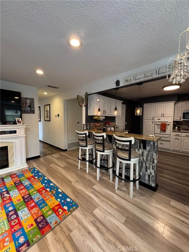 2835 Etiwanda Ave, Rialto, CA 92376 - kitchen with stainless steel microwave, wood finished floors, a peninsula, a textured ceiling, and a kitchen breakfast bar