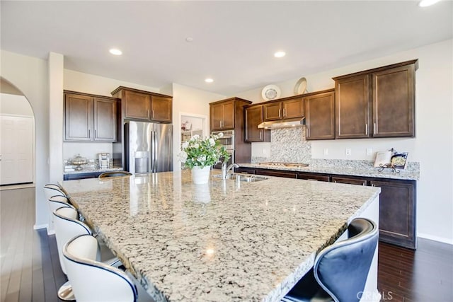 35212 Smith Ave, Beaumont, CA 92223 - kitchen featuring appliances with stainless steel finishes, under cabinet range hood, arched walkways, dark wood-style floors, and a large island with sink