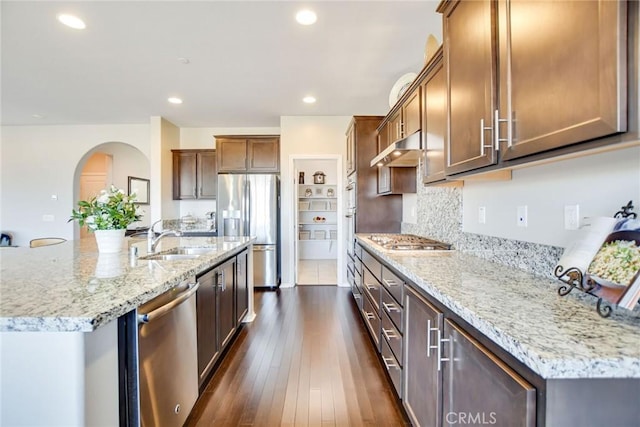 35212 Smith Ave, Beaumont, CA 92223 - kitchen with appliances with stainless steel finishes, under cabinet range hood, arched walkways, light stone countertops, and a kitchen island with sink