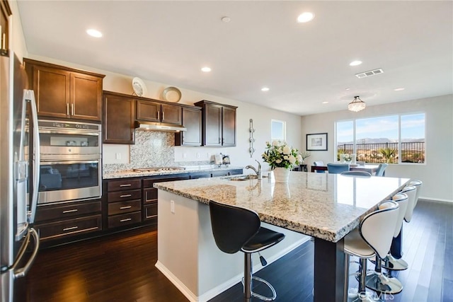 35212 Smith Ave, Beaumont, CA 92223 - kitchen with appliances with stainless steel finishes, a kitchen breakfast bar, dark wood-style floors, an island with sink, and light stone counters