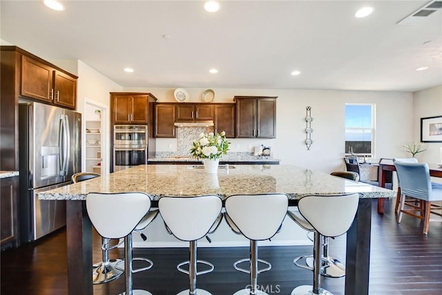 35212 Smith Ave, Beaumont, CA 92223 - kitchen featuring stainless steel appliances, a center island with sink, light stone countertops, a breakfast bar, and dark wood-style flooring