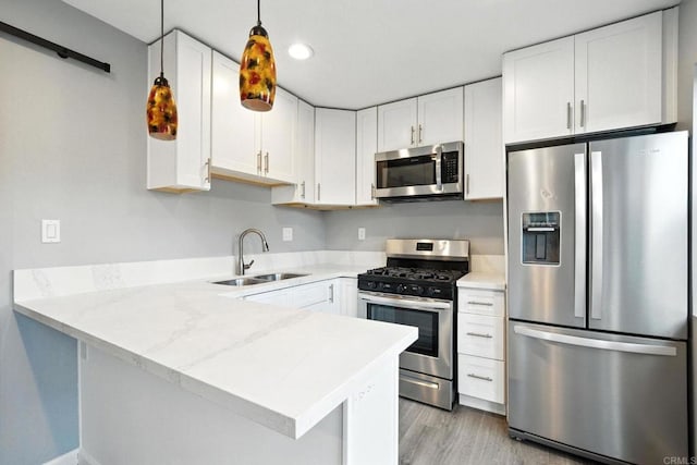 493133 Auburn, San Diego, CA 92105 - kitchen with appliances with stainless steel finishes, a peninsula, white cabinets, decorative light fixtures, and light wood-type flooring