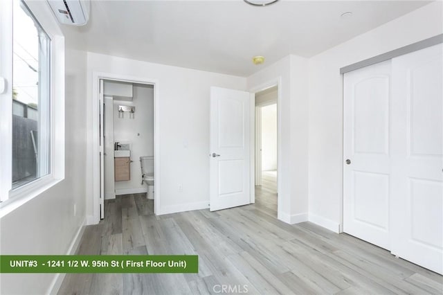 1241 W 95th St, Los Angeles, CA 90044 - unfurnished bedroom with light wood-style flooring, a closet, ensuite bathroom, and a wall mounted air conditioner