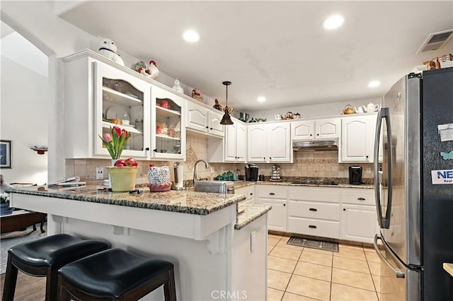 1115 Chennault Ave, Clovis, CA 93611 - kitchen featuring freestanding refrigerator, a peninsula, under cabinet range hood, glass insert cabinets, and stone counters