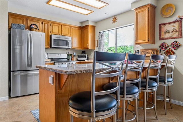 31941 Via Tafalla, Temecula, CA 92592 - kitchen featuring appliances with stainless steel finishes, light tile patterned floors, a breakfast bar, a peninsula, and dark stone counters