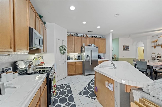 34722 Fairport Way, Yucaipa, CA 92399 - kitchen featuring appliances with stainless steel finishes, tile countertops, arched walkways, a kitchen island with sink, and light tile patterned flooring