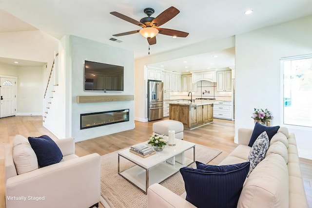 15716 Milne Cir, Moorpark, CA 93021 - living area featuring light wood finished floors, ceiling fan, a glass covered fireplace, stairs, and recessed lighting