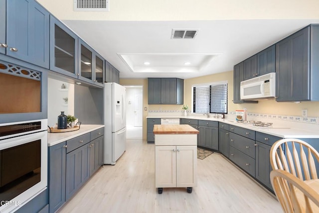 6357 Irena Ave, Camarillo, CA 93012 - kitchen with white appliances, light wood-style floors, a raised ceiling, glass insert cabinets, and wooden counters
