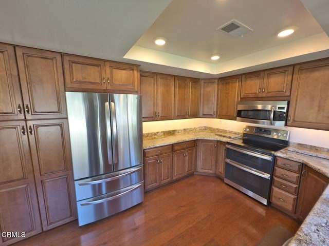 37134 Village 37, Camarillo, CA 93012 - kitchen featuring stainless steel appliances, a raised ceiling, brown cabinetry, dark wood-style floors, and light stone counters