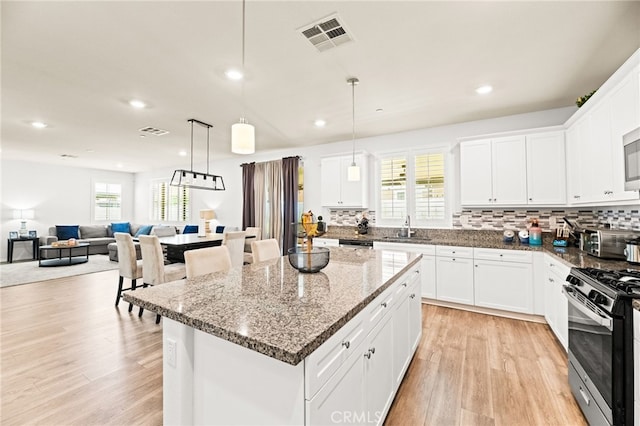 27555 Mountainside St, Menifee, CA 92584 - kitchen featuring gas range, light wood-style floors, a center island, decorative backsplash, and dark stone counters