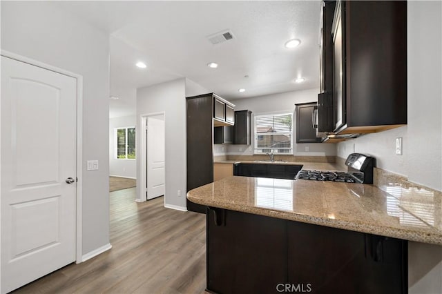 37398 Paseo Violeta Unit 75, Murrieta, CA 92563 - kitchen featuring gas range oven, a peninsula, light stone countertops, dark brown cabinets, and wood finished floors