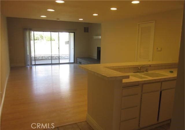 23551 Avenida La Caza Unit 129, Coto De Caza, CA 92679 - kitchen featuring light wood-style flooring, recessed lighting, open floor plan, white cabinetry, and tile counters