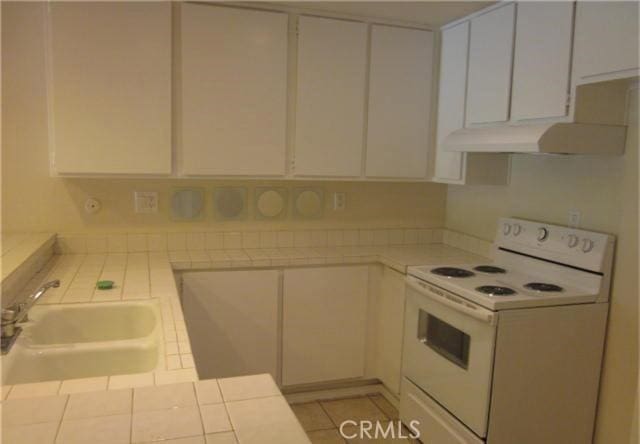 23551 Avenida La Caza Unit 129, Coto De Caza, CA 92679 - kitchen with white electric range, tile countertops, white cabinets, and under cabinet range hood