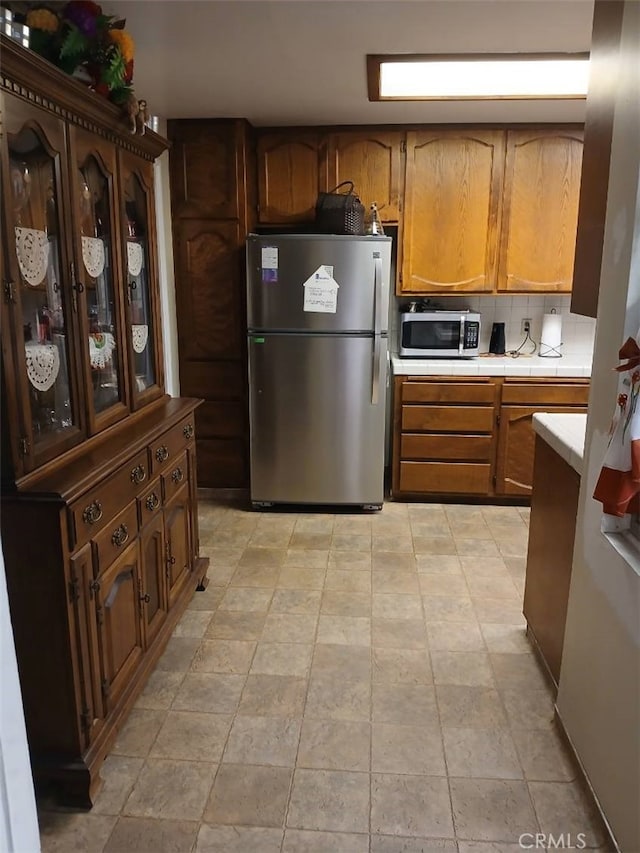 25521 17th St, San Bernardino, CA 92404 - kitchen featuring appliances with stainless steel finishes, tile countertops, brown cabinetry, and stone finish flooring