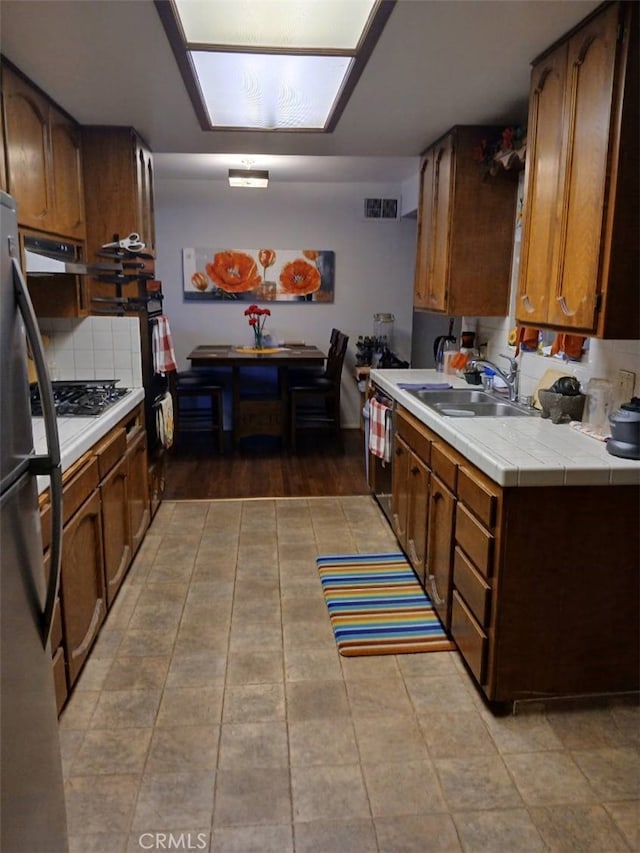 25521 17th St, San Bernardino, CA 92404 - kitchen featuring stainless steel appliances, exhaust hood, tile countertops, and brown cabinets