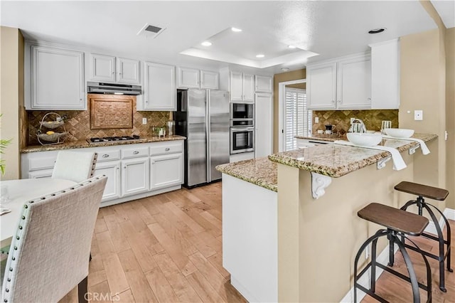 24676 Vista Cerritos, Calabasas, CA 91302 - kitchen featuring stainless steel appliances, white cabinets, a peninsula, a raised ceiling, and light wood-type flooring