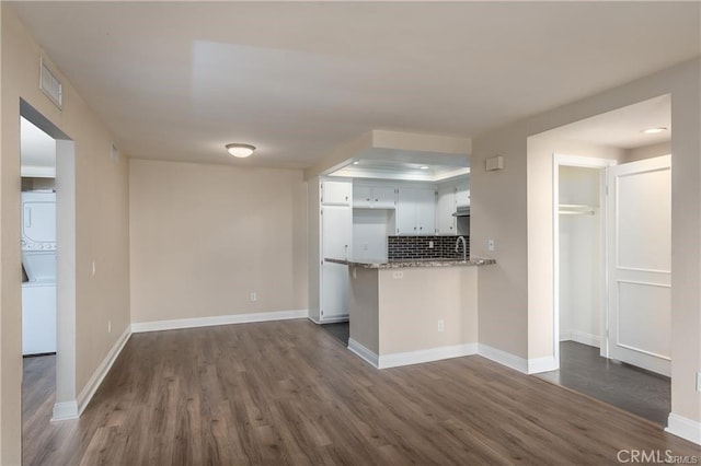 24297 El Pilar, Laguna Niguel, CA 92677 - kitchen featuring stacked washer and clothes dryer, dark wood-style flooring, a peninsula, tasteful backsplash, and white cabinetry