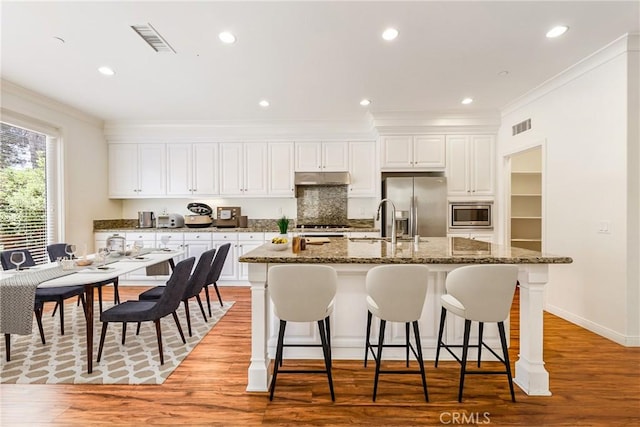 41 Somerton, Irvine, CA 92620 - kitchen featuring appliances with stainless steel finishes, a kitchen island with sink, ornamental molding, a breakfast bar, and white cabinetry