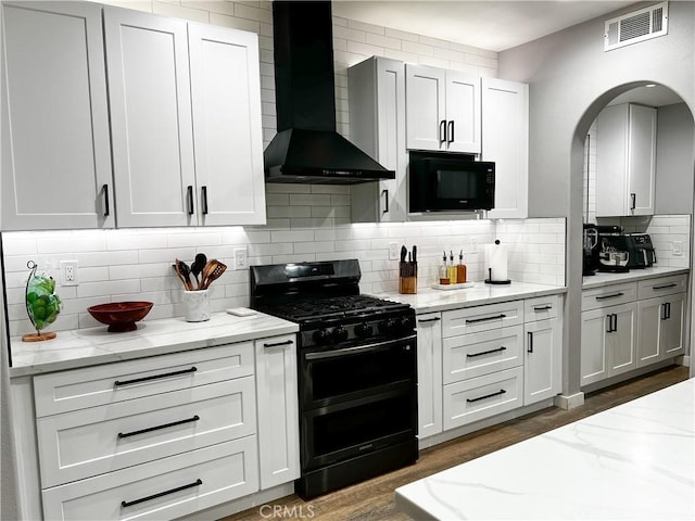 5834 Gem Ct, Lancaster, CA 93536 - kitchen with black appliances, wall chimney range hood, backsplash, arched walkways, and light stone counters