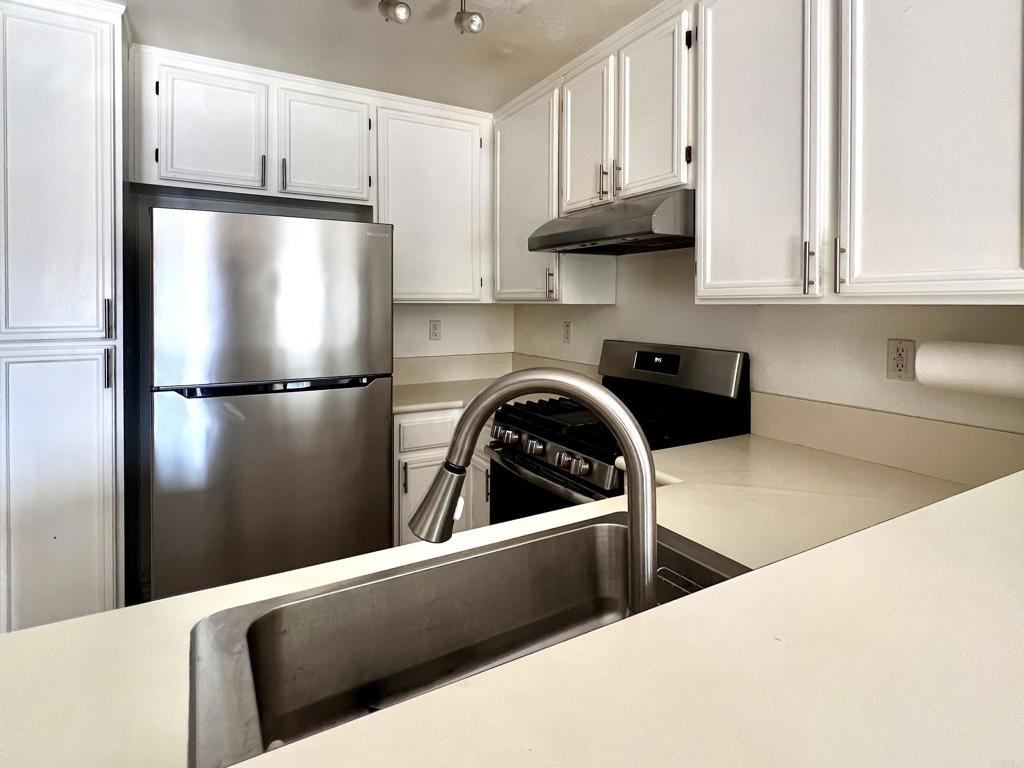 506 62nd St Unit 5, San Diego, CA 92114 - kitchen with appliances with stainless steel finishes, under cabinet range hood, light countertops, and white cabinets