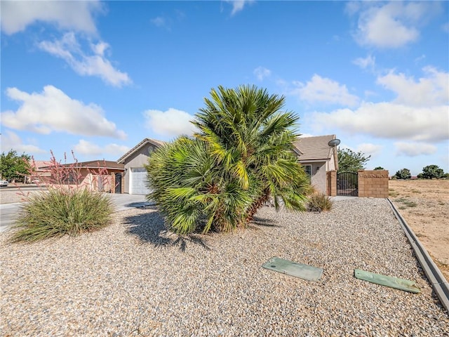 27239 Peach Tree Ln, Helendale, CA 92342 - view of property hidden behind natural elements with a gate, an attached garage, stucco siding, and driveway