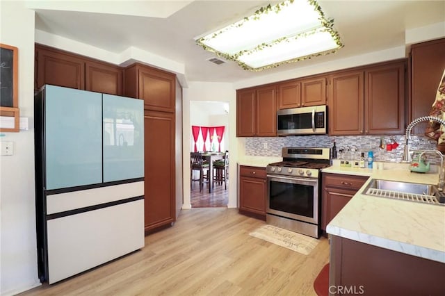 4242 Trenton Ave, Palmdale, CA 93552 - kitchen with stainless steel appliances, tasteful backsplash, light countertops, light wood-type flooring, and brown cabinetry