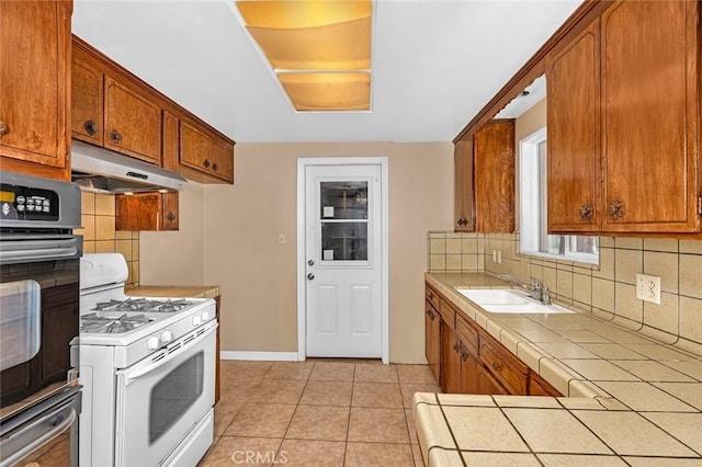 45660 Shain Ave, Dos Palos, CA 93620 - kitchen with white range with gas stovetop, under cabinet range hood, black oven, tile countertops, and tasteful backsplash