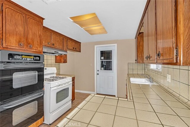 45660 Shain Ave, Dos Palos, CA 93620 - kitchen featuring white gas range, under cabinet range hood, tasteful backsplash, and brown cabinets