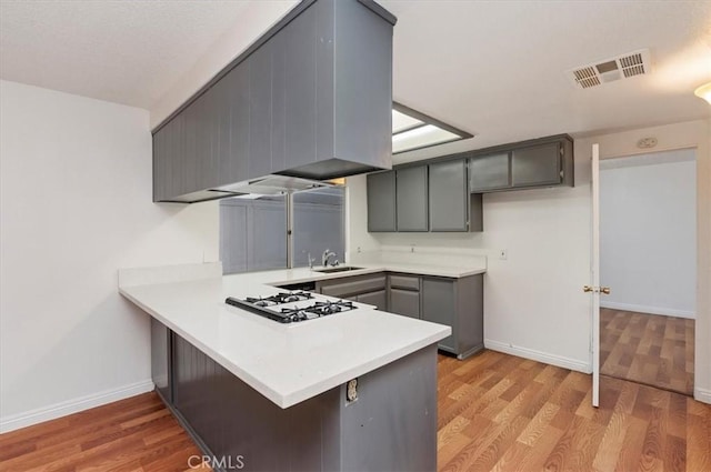 23405 Ramona Ave, Apple Valley, CA 92307 - kitchen with white gas stovetop, a peninsula, light countertops, and light wood-style flooring