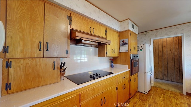 125 Hilton St, Madera, CA 93637 - kitchen with black appliances, under cabinet range hood, wallpapered walls, light wood-style floors, and decorative backsplash