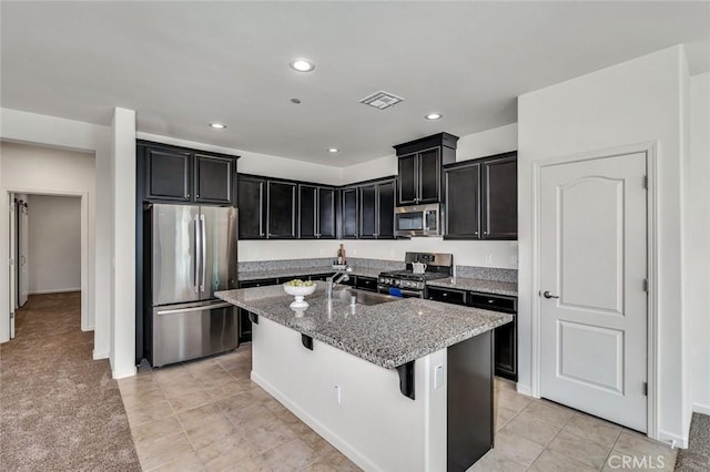 860 Fritz Dr, Los Banos, CA 93635 - kitchen with stainless steel appliances, dark cabinets, stone counters, a breakfast bar area, and a center island with sink