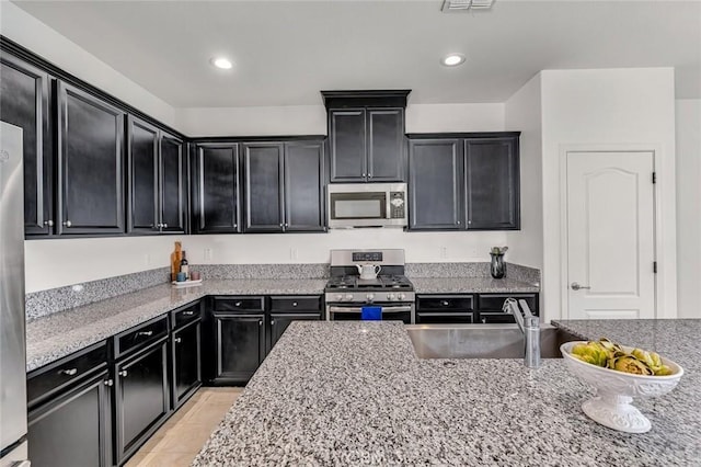 860 Fritz Dr, Los Banos, CA 93635 - kitchen with stainless steel appliances, dark cabinets, light stone countertops, light tile patterned floors, and recessed lighting