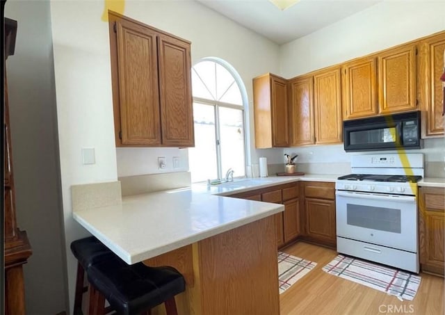 6287 Tuckaway Ave, Banning, CA 92220 - kitchen with black microwave, white range with gas stovetop, light wood-type flooring, and a peninsula