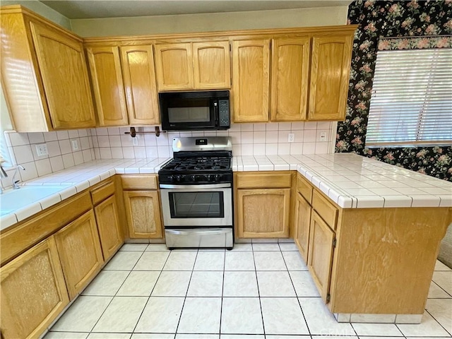 224 Stonewood Dr, Los Banos, CA 93635 - kitchen with black microwave, gas stove, a peninsula, tasteful backsplash, and light tile patterned flooring