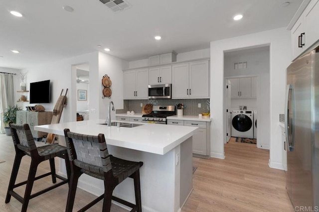 2051 Julie Dawn Pl, Escondido, CA 92026 - kitchen featuring washer and dryer, stainless steel appliances, a breakfast bar area, light wood-style flooring, and backsplash
