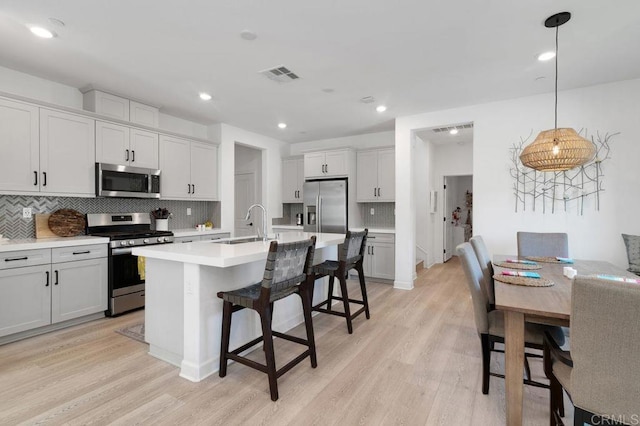 2051 Julie Dawn Pl, Escondido, CA 92026 - kitchen featuring appliances with stainless steel finishes, light wood-type flooring, tasteful backsplash, a kitchen breakfast bar, and light countertops
